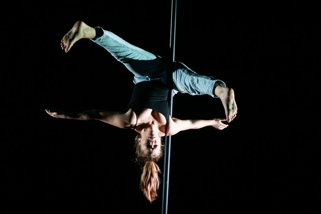 A performer balances upside down on a pole.