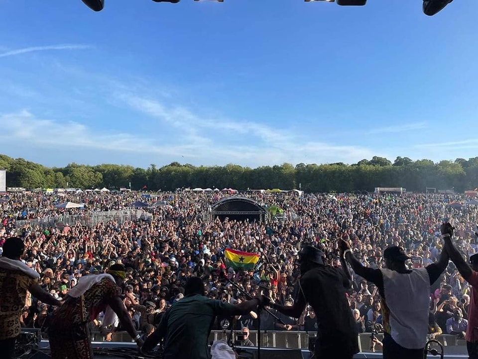 A new era for Africa Oyé begins in 2026 with Earlybird festival tickets on sale A band take a bow in front of a packed festival crowd underneath a blue sky.