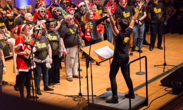 A choir in Christmas hats being conducted during a performance,